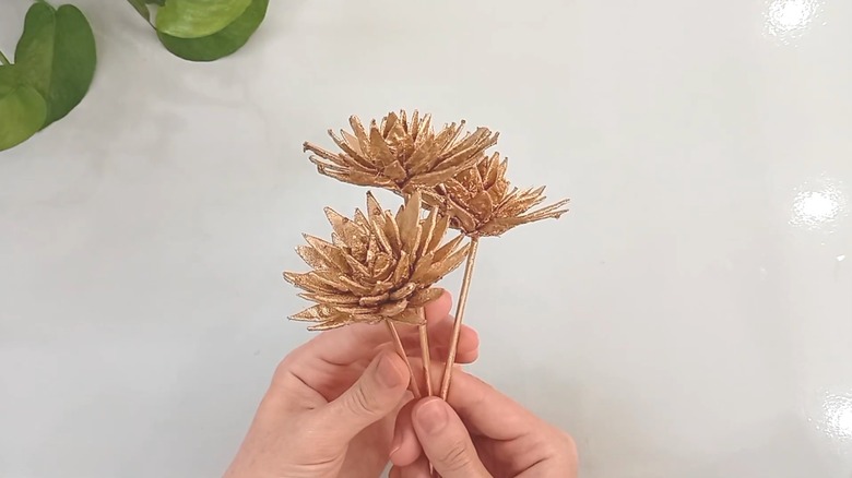 Hands holding gold cardboard paper flowers made from egg cartons and skewers over a glossy white countertop