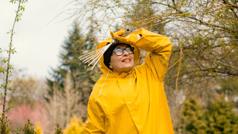 A woman in a yellow raincoat looks out for rain in a backyard