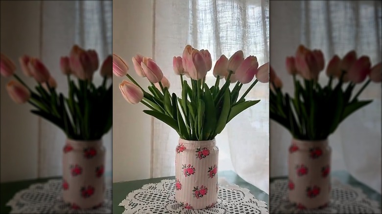 A decoupaged pickle jar used as a vase for pink roses.