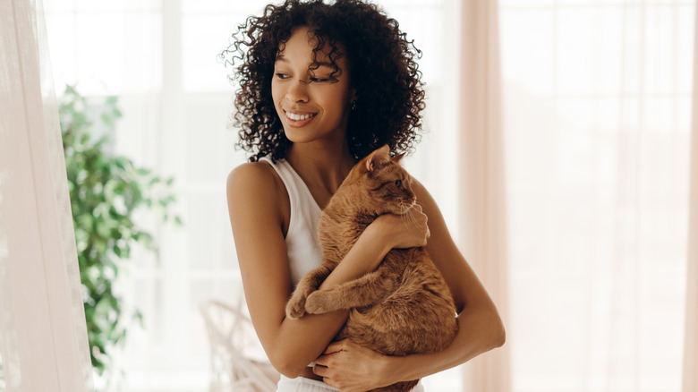 A woman smiles while holding her orange cat