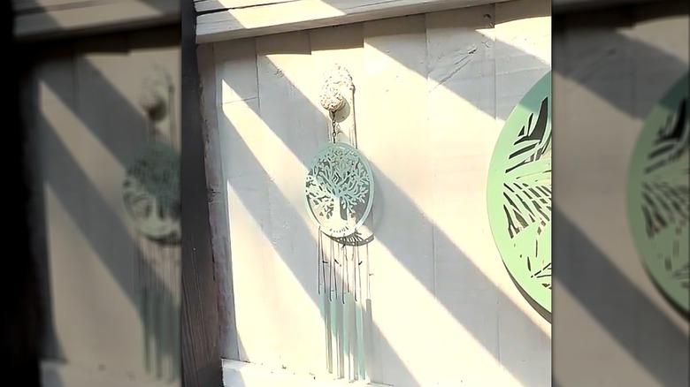 Outdoor metal wind chime shaped like a tree hanging on vintage white door knob on fence