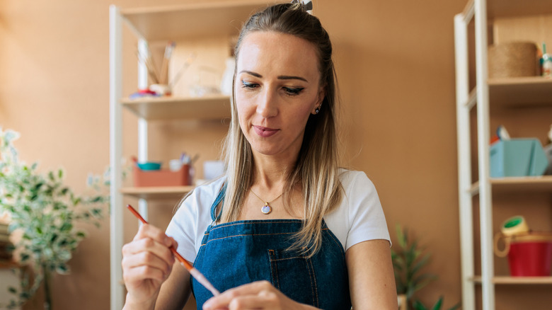 A woman holds a paintbrush, getting ready to craft.