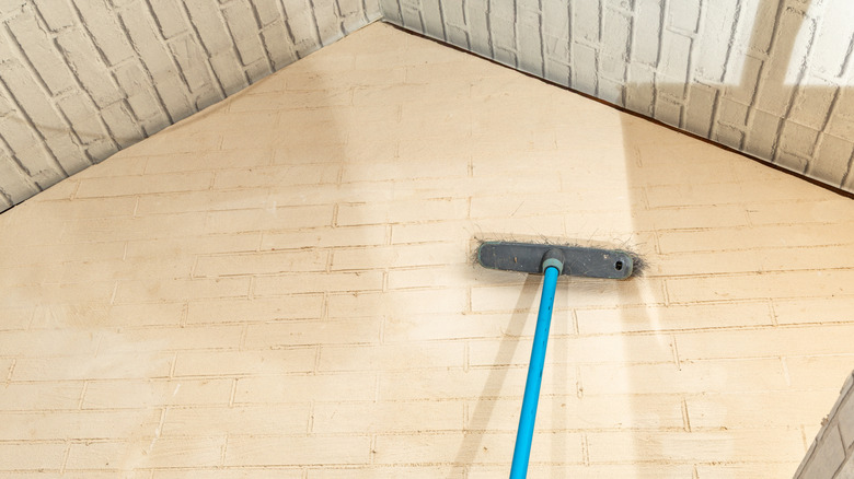 Using a long-handled broom to remove cobwebs