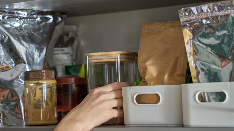 Person reaching for a container on a wood pantry shelf