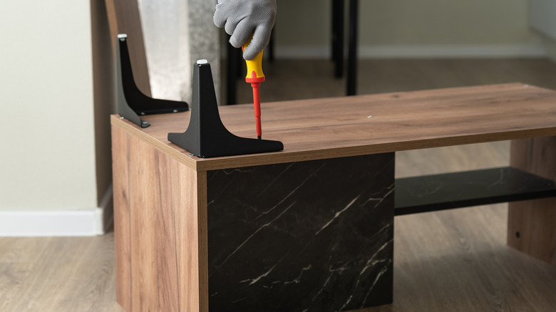 Gloved male hand using a screwdriver to tighten the legs of a table