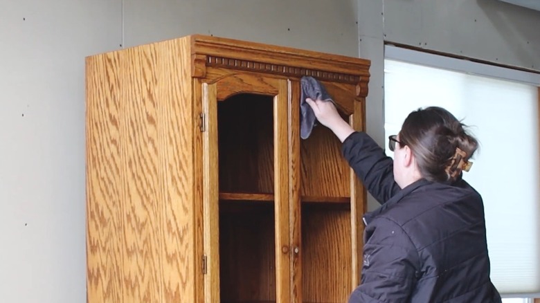 Woman with glasses and claw clip preparing a vintage honey oak hutch for remodeling project at home