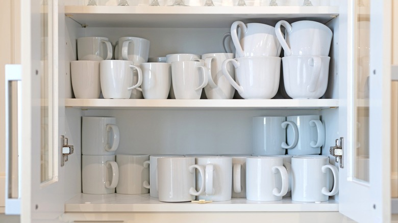White kitchen cabinet full of stacked coffee mugs