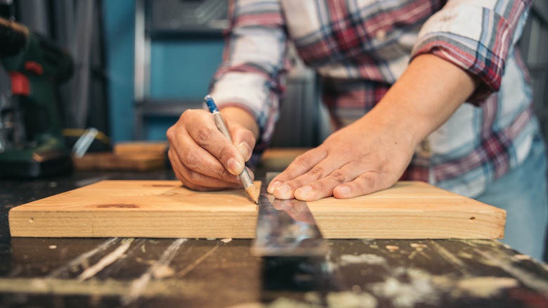 A person uses a ruler to mark a board of scrap wood