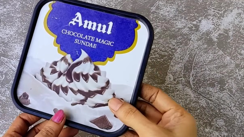 Person holding a square plastic ice cream lidd