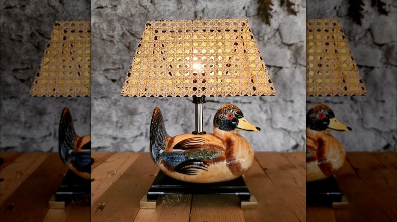 A thrifted duck figurine lamp with a cane lampshade sits on a wooden table
