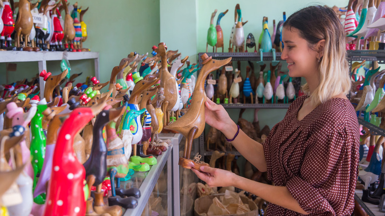 A woman smiles while looking at a wooden duck sculpture