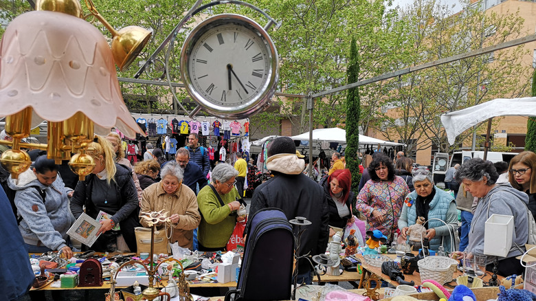 A crowd of people look at a large assortment of flea market wares