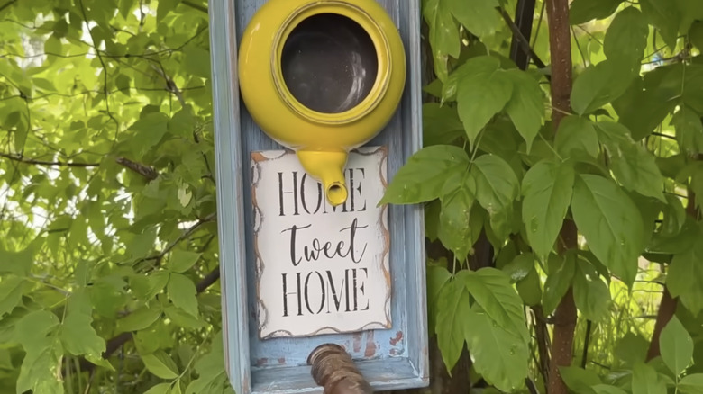 A yellow teapot hangs inside a wooden drawer above a sign that reads "Home Tweet Home"