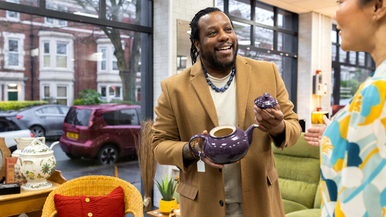 A man holds a teapot in a thrift store