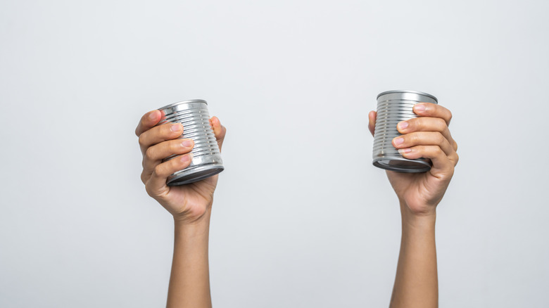 hands holding tin cans