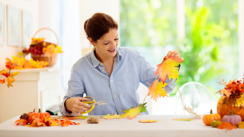 A smiling woman makes fall decor using colorful orange faux leaves
