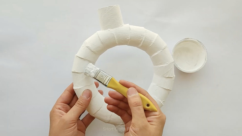 A person's hands painting DIY toilet paper roll vase with white paint