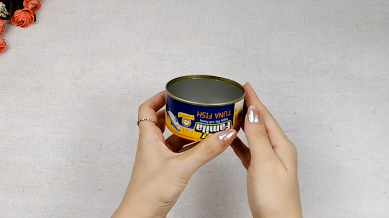 Person holding an empty tuna can over a work surface