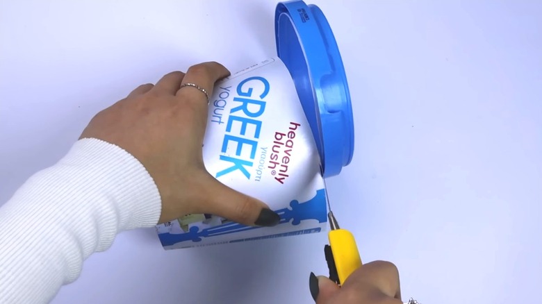 Person cutting the top off a yogurt container on a work surface