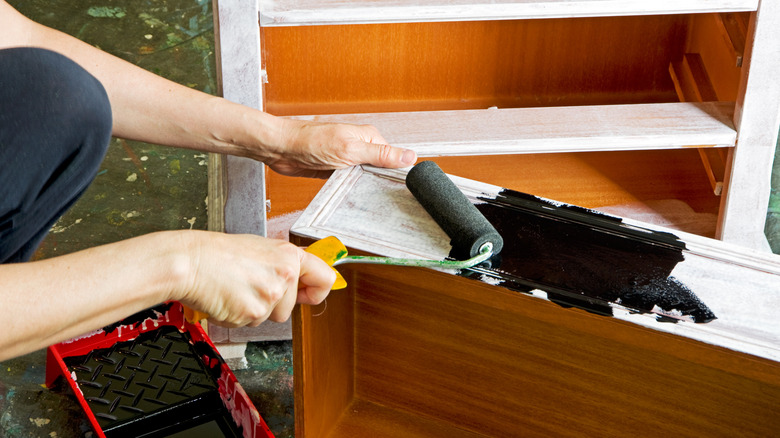 Person painting the drawer of a dresser