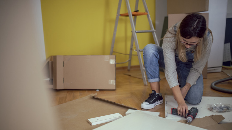 Woman building flatpack cabinet with cordless drill