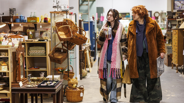 Two people walking through a thrift shop near a display of baskets