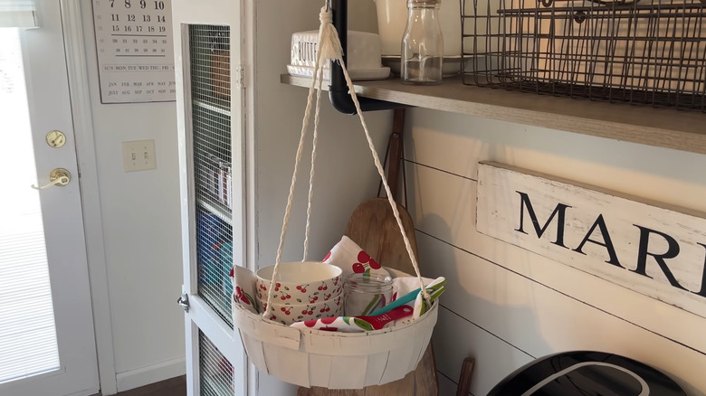 Round basket hanging from braided cords filled with cherry-themed kitchen decor