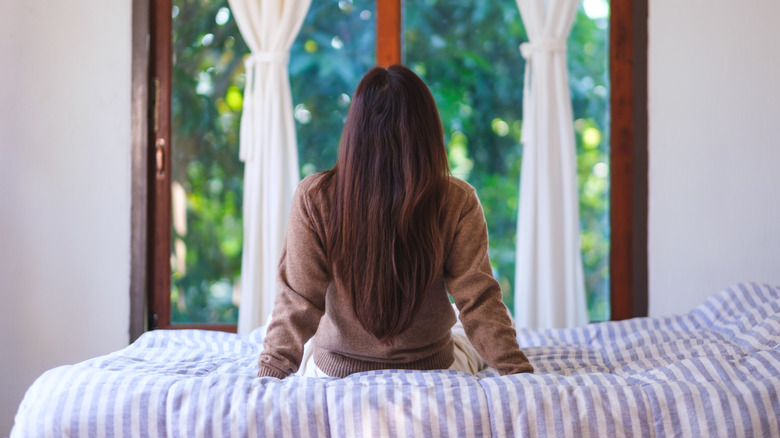 Woman sitting on bed looking outside at garden