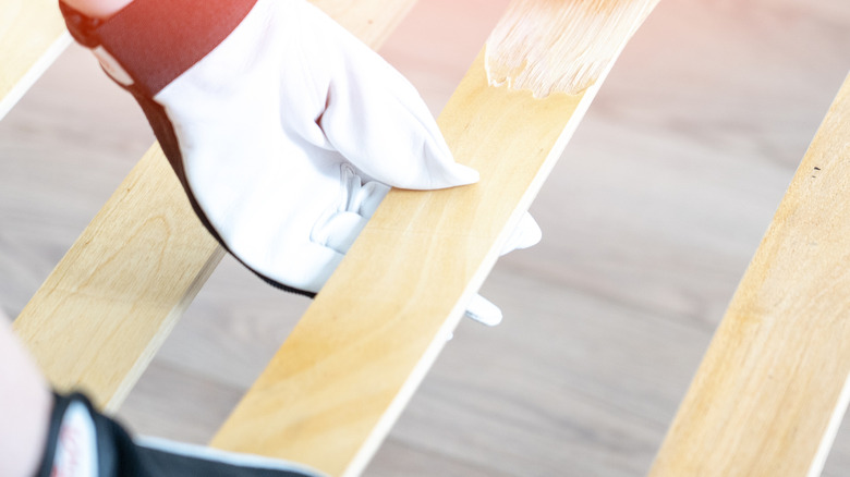 A gloved hand holds onto a partially painted wood slat