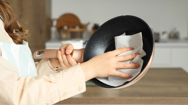 A person wipes a frying pan with a cloth