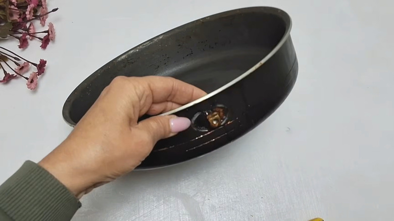 Hand with painted pink nails holding up old frying pan