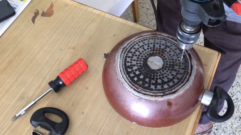 Person drilling holes into an old frying pan to make a succulent planter
