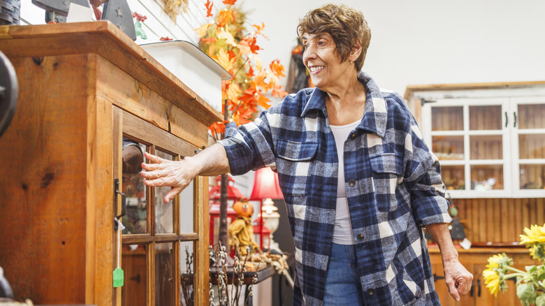 An older woman smiles while looking at thrift store furniture