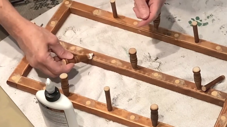 Woman upcycling magazine rack by re-attaching spindles as hooks for mug rack DIY on worktable