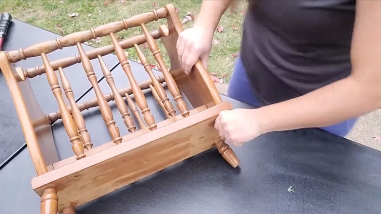 Woman disassembling vintage wood magazine rack with tall spindles on outdoor table