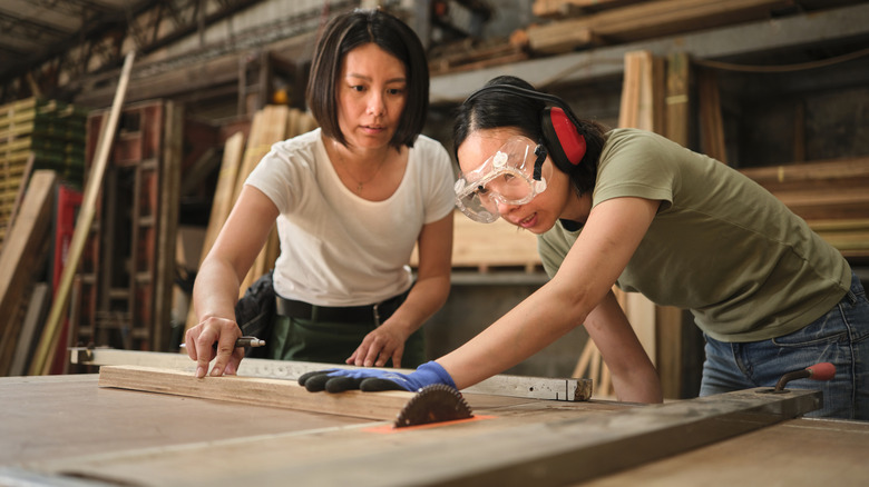 Two people working together to cut a wood board with a table saw