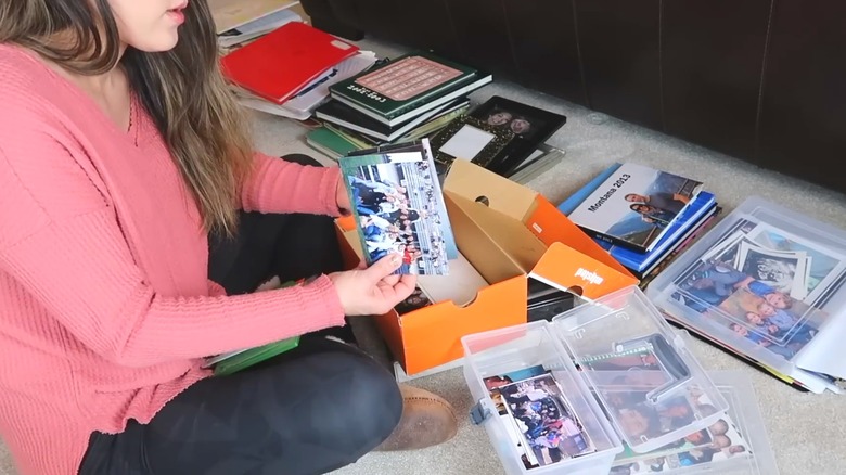 Young woman sorting through keepsake photos and books with open orange shoebox