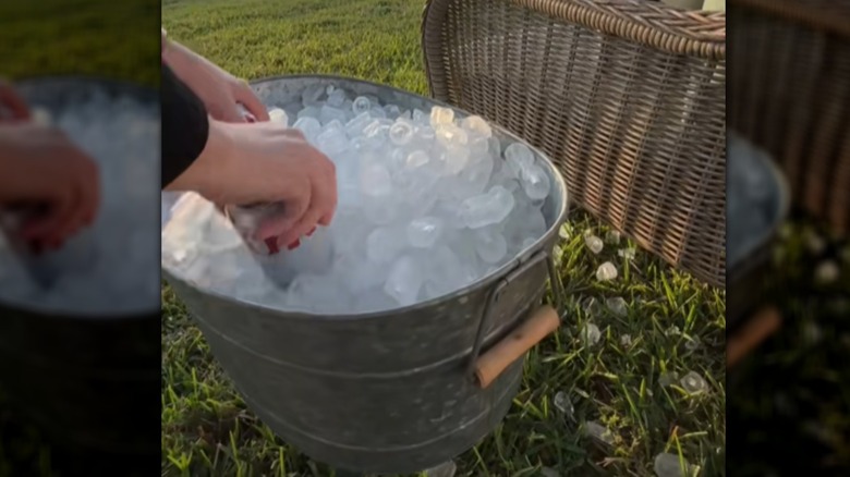 Person putting drinks in a galvanized bucket filled with ice that's attached to a wood stool