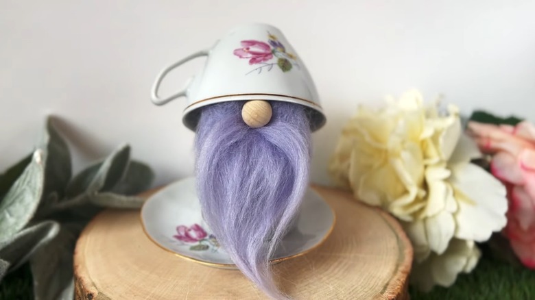 Lilac handmade gnome sandwiched between teacup and saucer set as eccentric decor