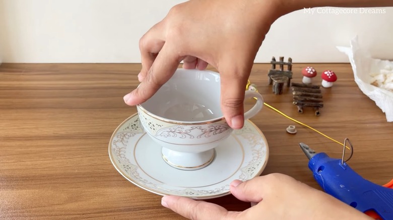 Woman hot gluing teacup set for DIY project with fairy garden embellishments on wood table