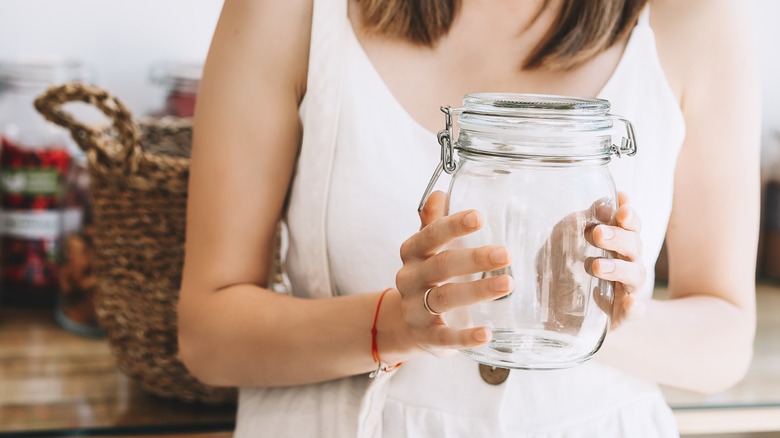 Person holding empty glass jar with lid.