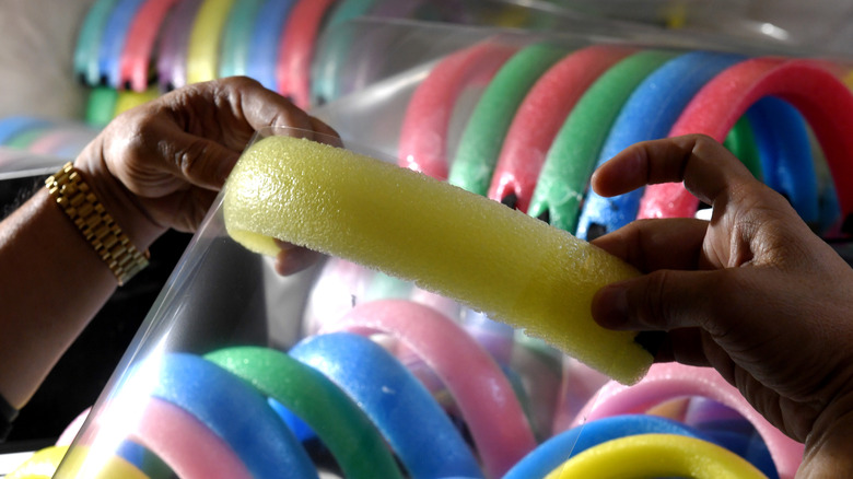 A person's hands are shown bending a yellow pool noodle