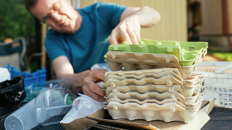 A person looking through a stack of empty egg cartons