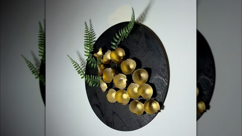 A piece of decorative art made of gold-painted eggshells and faux greenery hang on a white wall