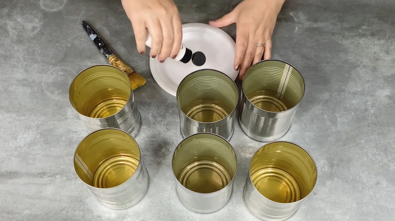 Woman pouring paint onto plate to redesign soup cans for DIY caddy
