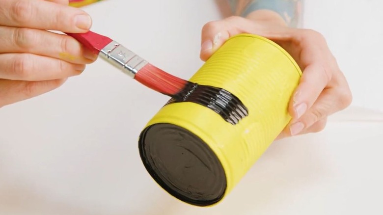 Woman painting soup can to turn into garden decor