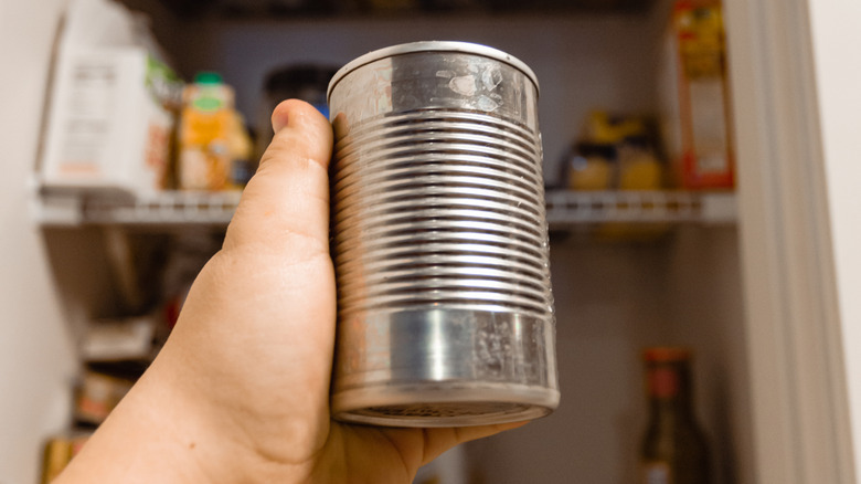 Hand holding soup can without label in front of pantry