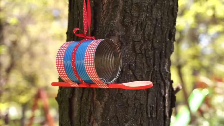 Soup can bird feeder painted blue and decorated with red ribbon hanging in a tree