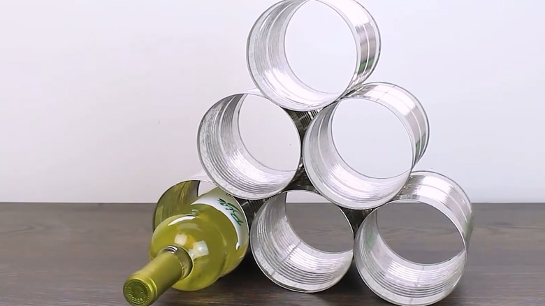 White wine bottle tucked into DIY soup can rack on gray wood table with empty background