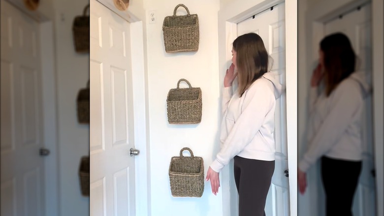Young woman showing off trio of wicker basket wall decor in white hallway